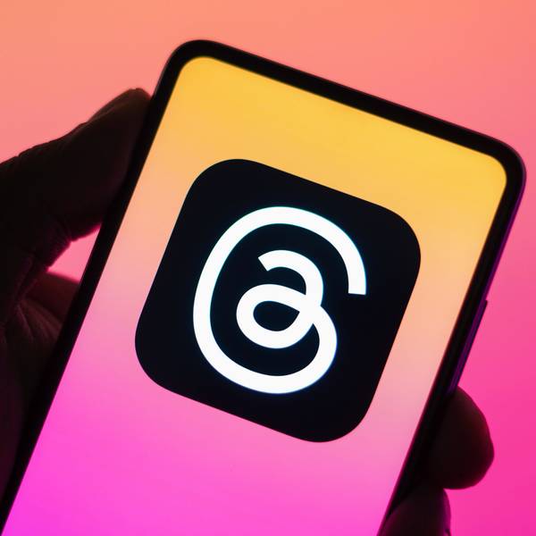 Das Threads-Logo ist auf einem Handy zu sehen, das vor eine bunte Wand gehalten wird.