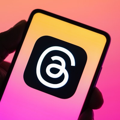 Das Threads-Logo ist auf einem Handy zu sehen, das vor eine bunte Wand gehalten wird.