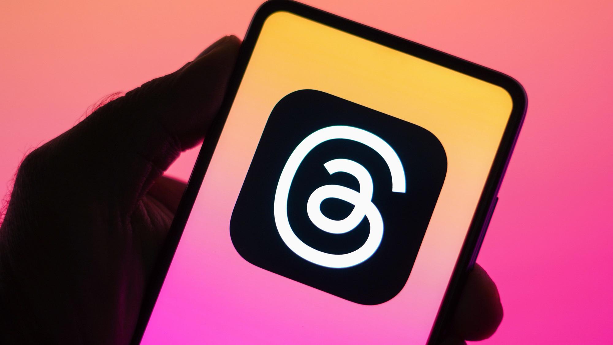Das Threads-Logo ist auf einem Handy zu sehen, das vor eine bunte Wand gehalten wird.