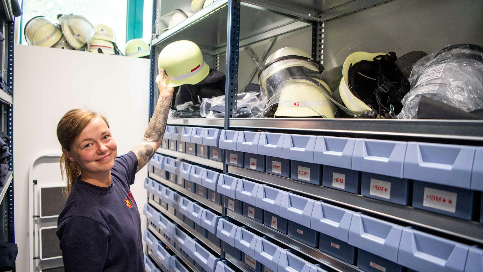 Eine Feuerwehrfrau steht in der Euskirchener Kleiderkammer und hält einen Helm in der Hand.