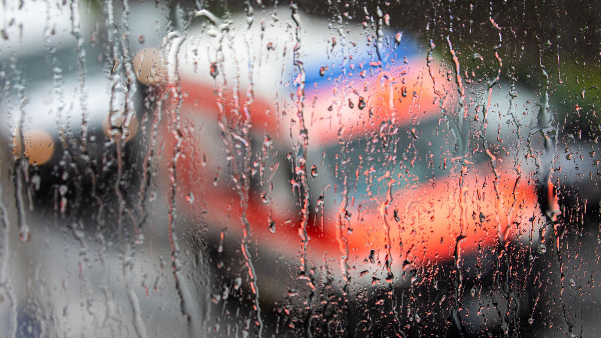 Ein Rettungswagen ist hinter einer Fensterscheibe zu sehen auf der sich während eines Unwetters mit Gewitter und Starkregen im Ortsteil Sülz zahlreiche Regentropfen gesammelt haben.