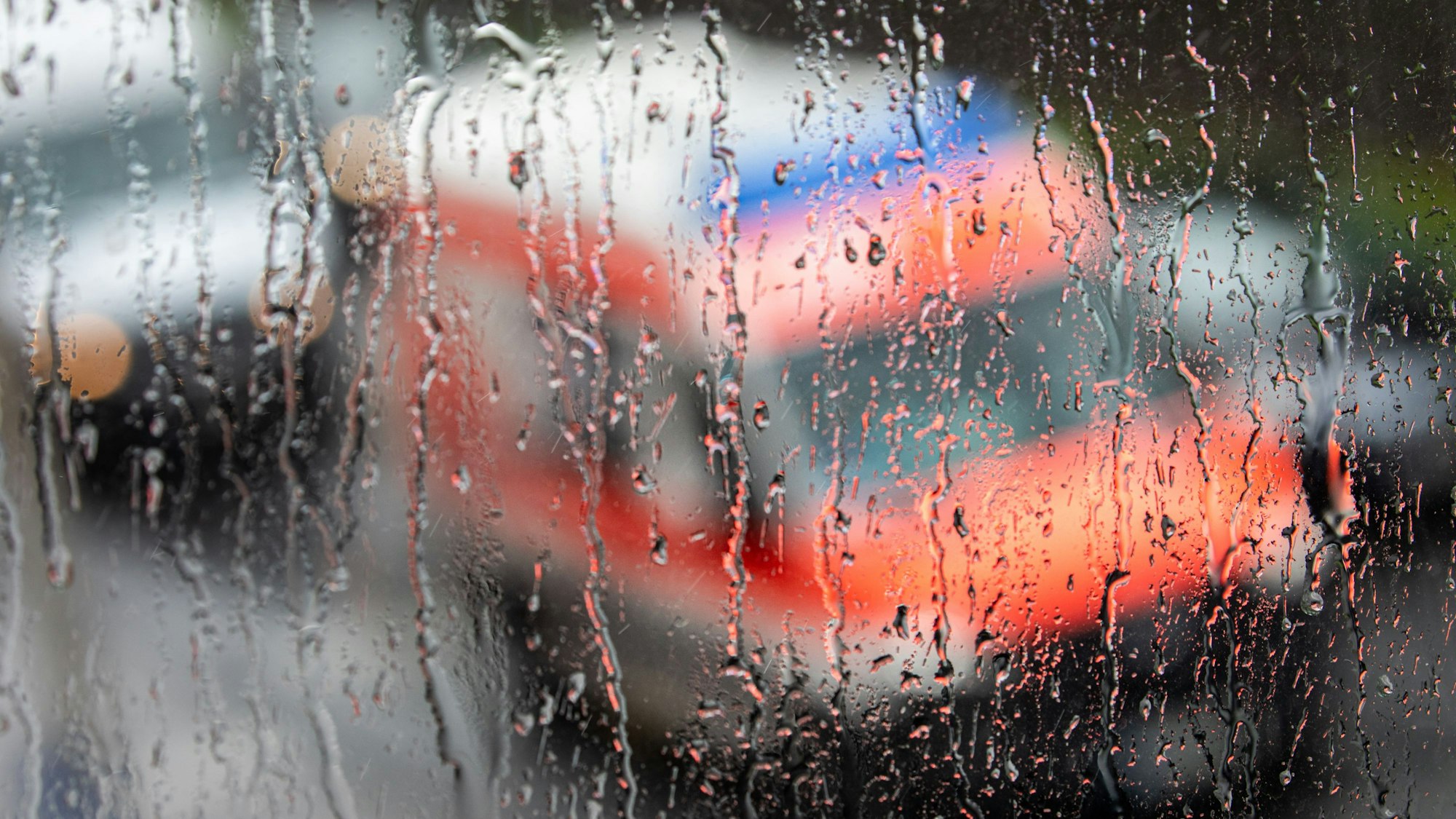 Ein Rettungswagen ist hinter einer Fensterscheibe zu sehen auf der sich während eines Unwetters mit Gewitter und Starkregen im Ortsteil Sülz zahlreiche Regentropfen gesammelt haben.