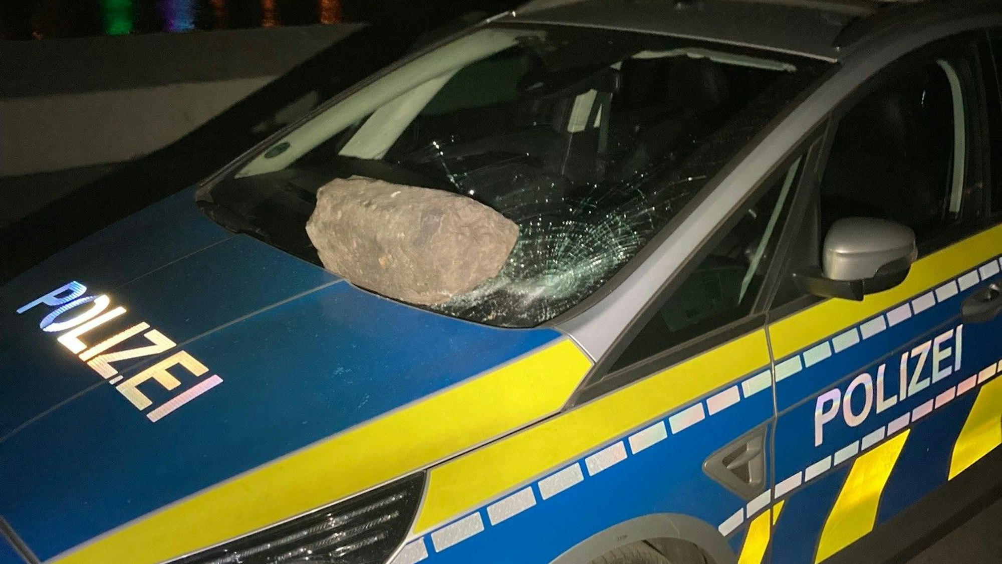 Ein schwerer Stein liegt auf der beschädigten Windschutzscheibe eines Streifenwagens.