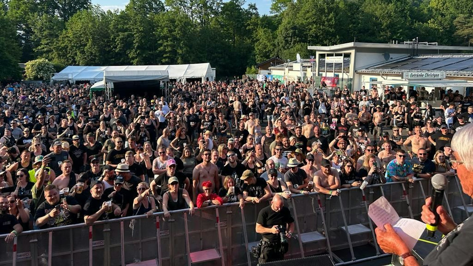 Eine Frau spricht auf der Bühne zum Publikum. Sie hält ein Mikrofon und ein Blatt Papier in der Hand.