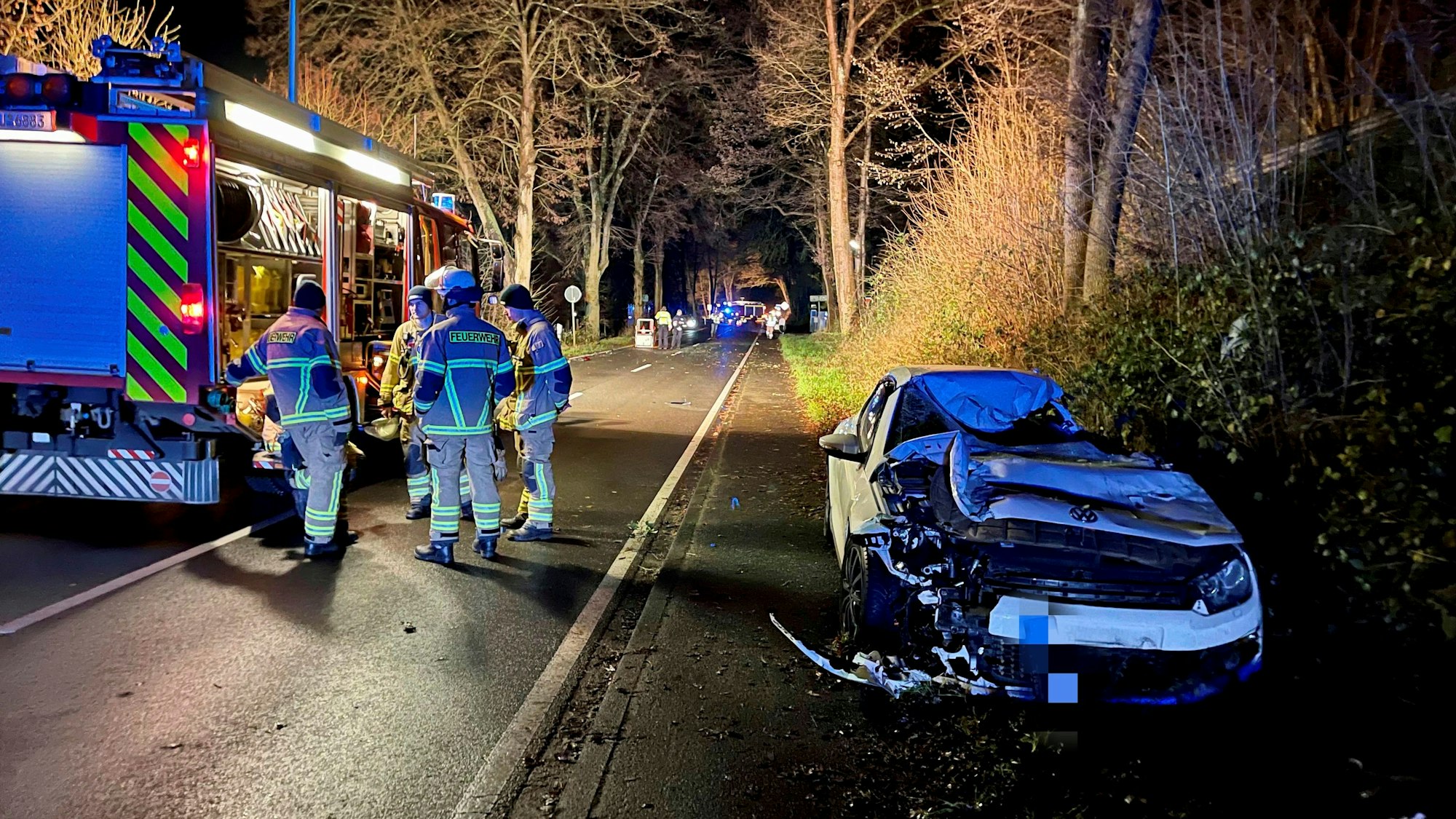 Ein demolierter VW Scirocco steht am Straßenrand. Mehrere Feuerwehrleute sind an der Unfallstelle auf der Wahnbachtalstraße im Much.