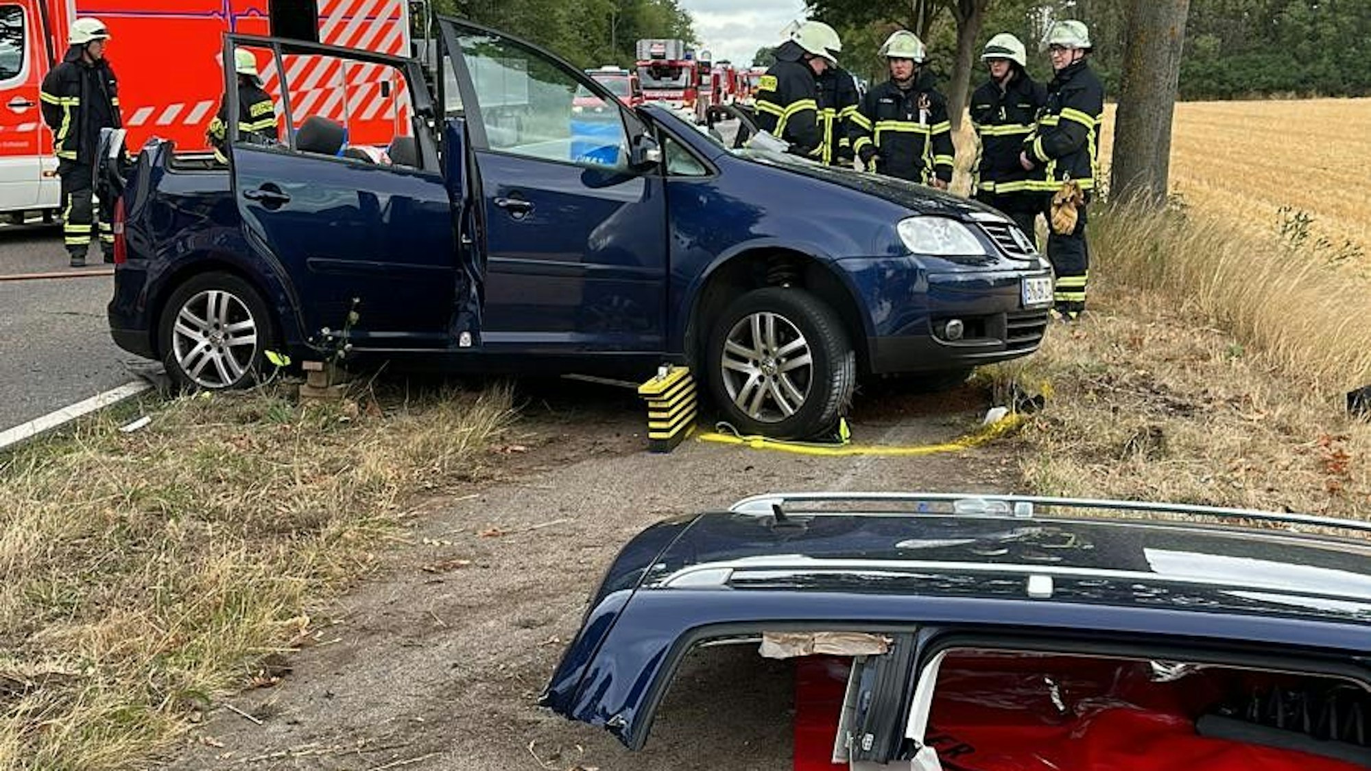 Ein Auto steht auf einem Seitenstreifen, das Dach liegt davor. Dahinter stehen Feuerwehrleute.