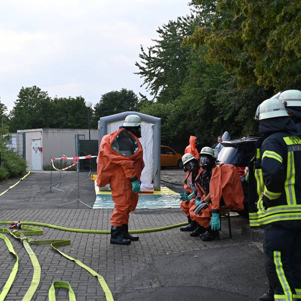 Feuerwehrleute in Schutzanzügen stehen und sitzen vor dem Bad, Schläuche sind ausgerollt.