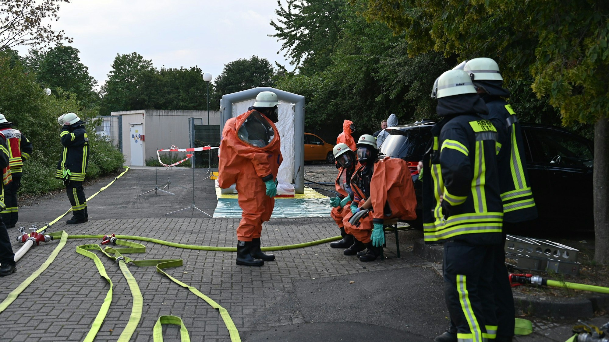 Feuerwehrleute in Schutzanzügen stehen und sitzen vor dem Bad, Schläuche sind ausgerollt.