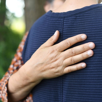 Ein Mensch legt tröstend seine Hand auf den Rücken eines jungen Menschen.