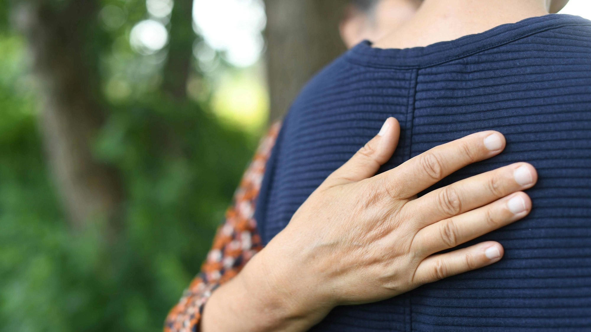 Ein Mensch legt tröstend seine Hand auf den Rücken eines jungen Menschen.