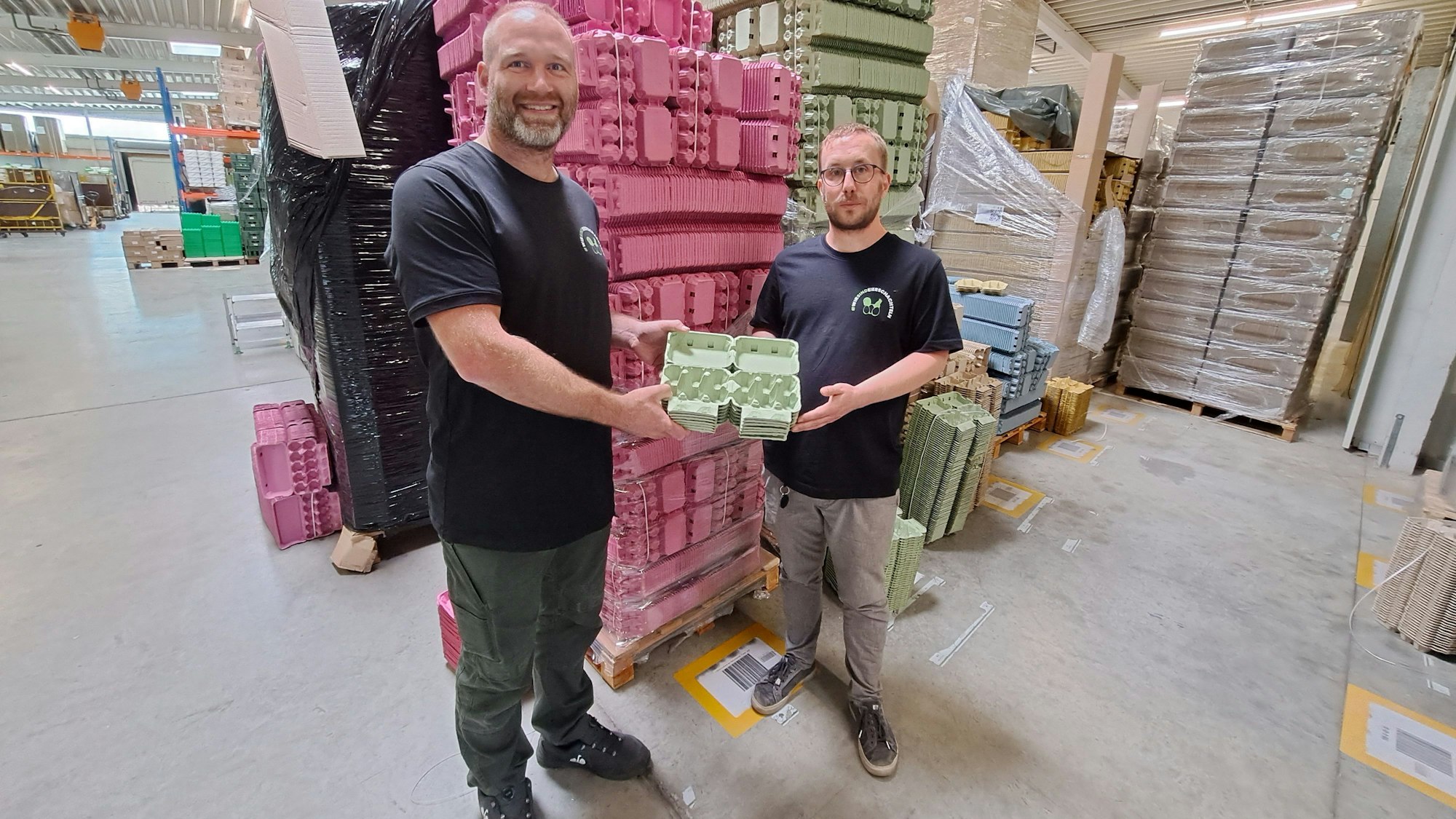 Firmengründer Meik Klose (rechts) und sein Geschäftspartner Daniel Debus stehen im Lager ihres Unternehmens eierschateln.de vor tausenden Eierkartons in unterschiedlichen Farben.