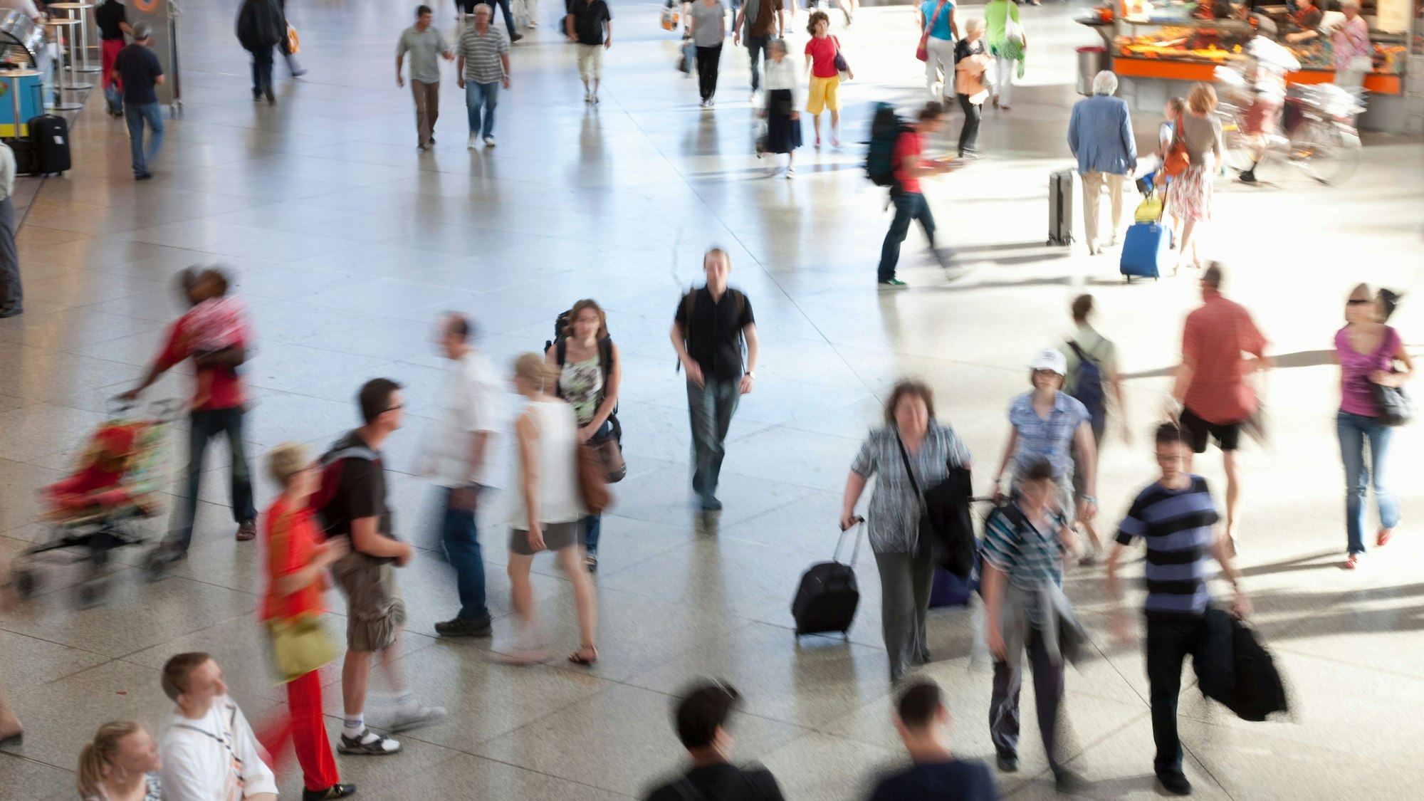 Ein junger Mann geht durch eine Bahnhofshalle, viele Menschen sind zu sehen, sie tragen sommerliche Kleidung. (Symbolbild)