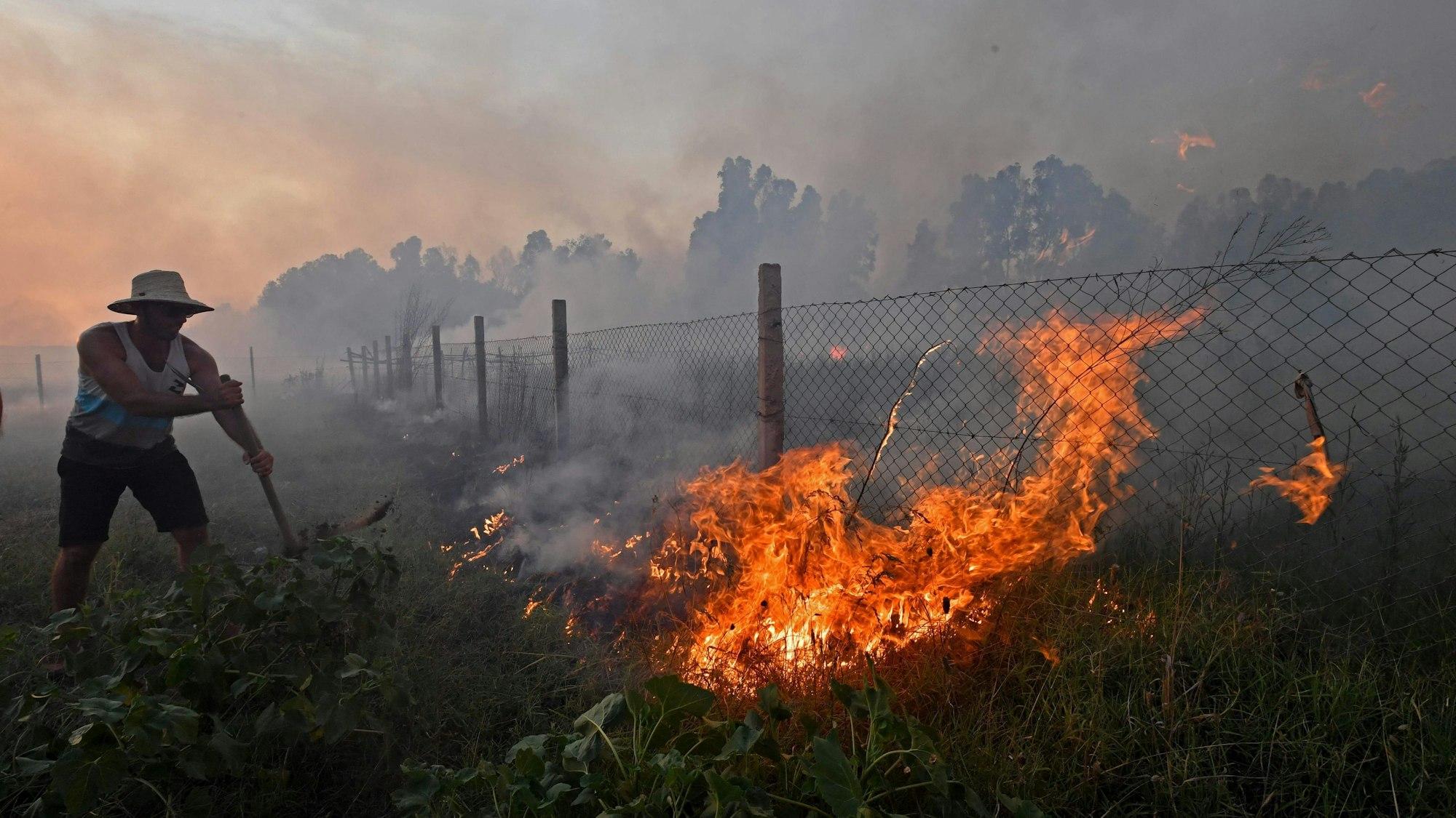 Ein Mann steht neben einem brennenden Zaun.