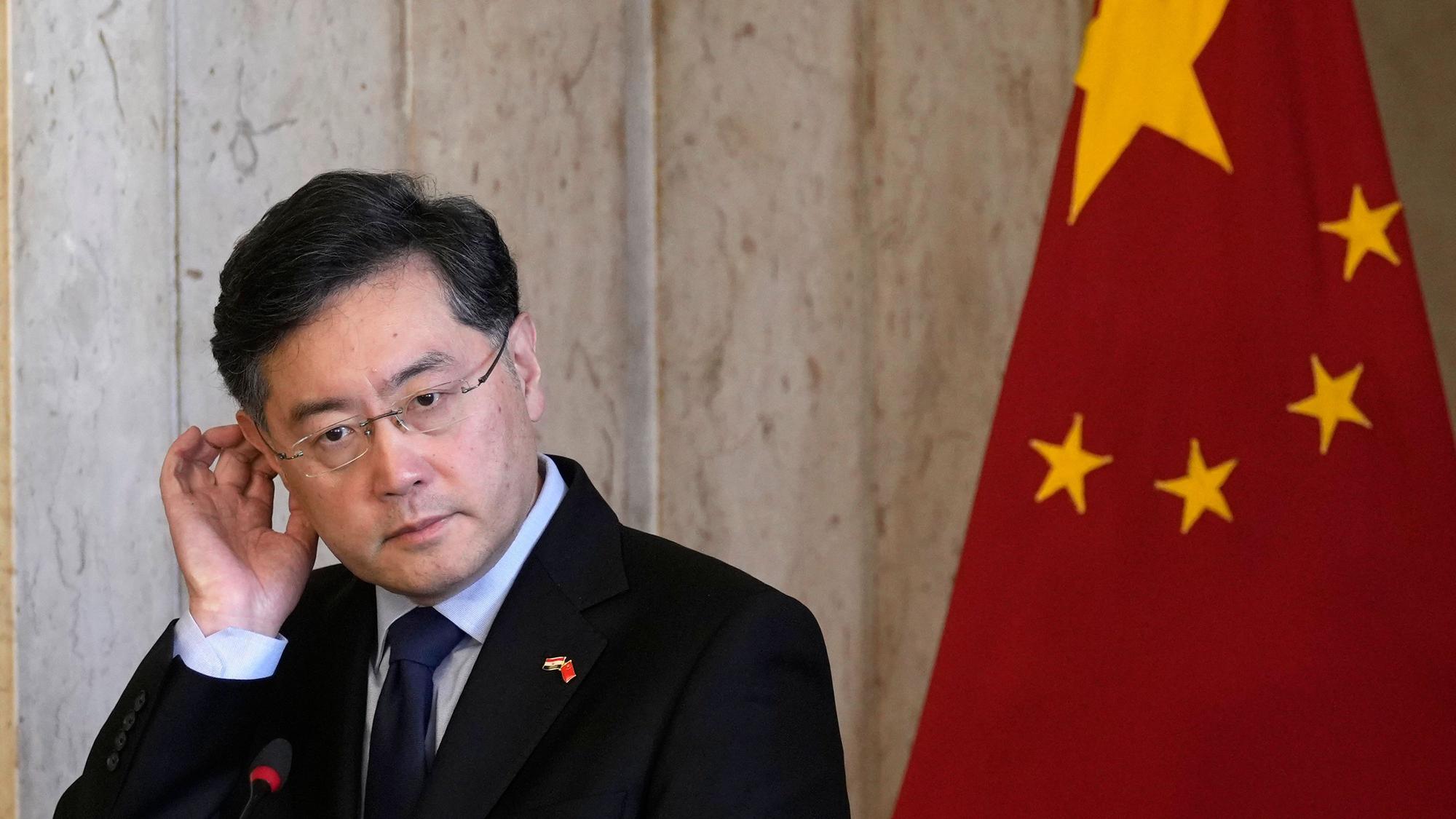 Der verschwundene ehemalige Außenminister von China, Qin Gang, kratz sich am Ohr - im Hintergrund ist eine chinesische Landesflagge zu sehen.
