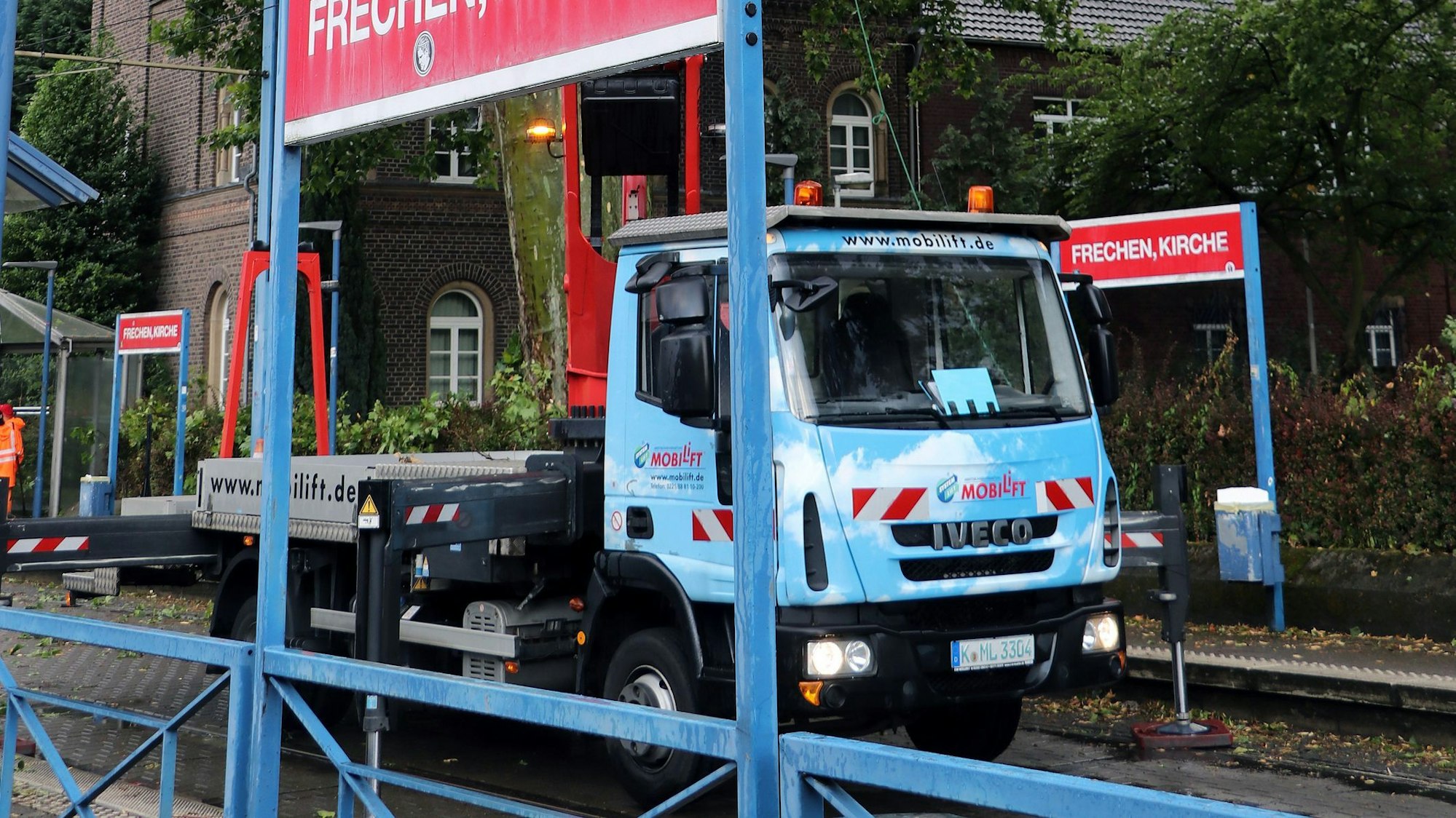 Das Bild zeigt die Haltestelle Frechen-Kirche und einen Hubwagen, von dem aus Arbeiter Äste aus dem Baum schneiden.