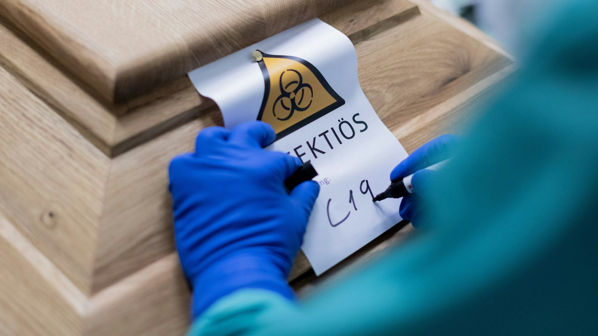 Ein Bestattungsunternehmer schreibt „C19“ auf ein Schild mit dem Hinweis „Infektiös“ auf einen Sarg mit einem Verstorbenen, der an dem Coronavirus gestorben ist.