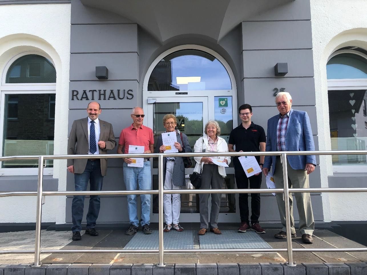 Bürgermeister Christoph Nicodemus (l..) steht mit Overather Bürgerinnen und Bürgern vor dem Rathaus-Eingang.