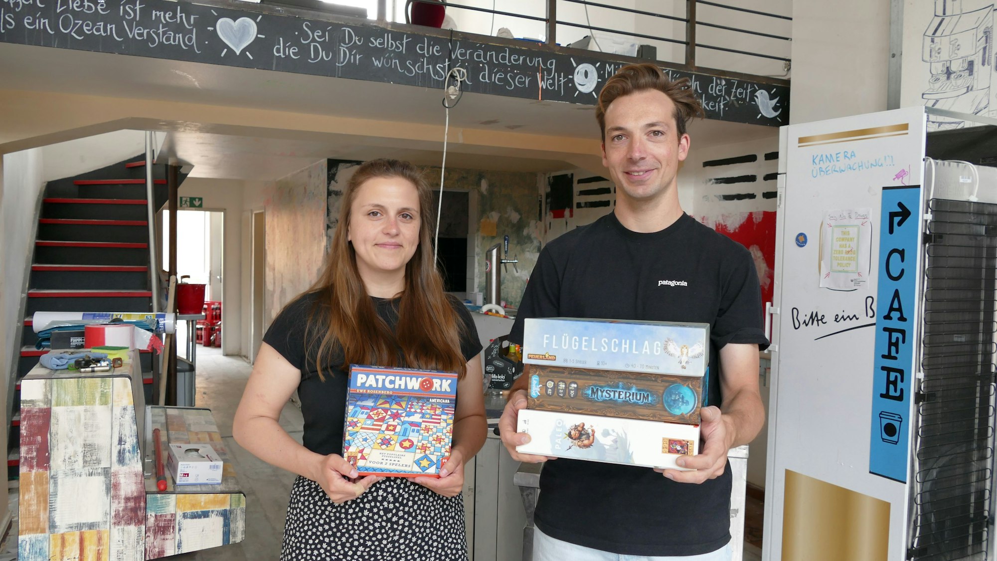 Die beiden Gründer stehen in dem Café mit Spielen in der Hand.