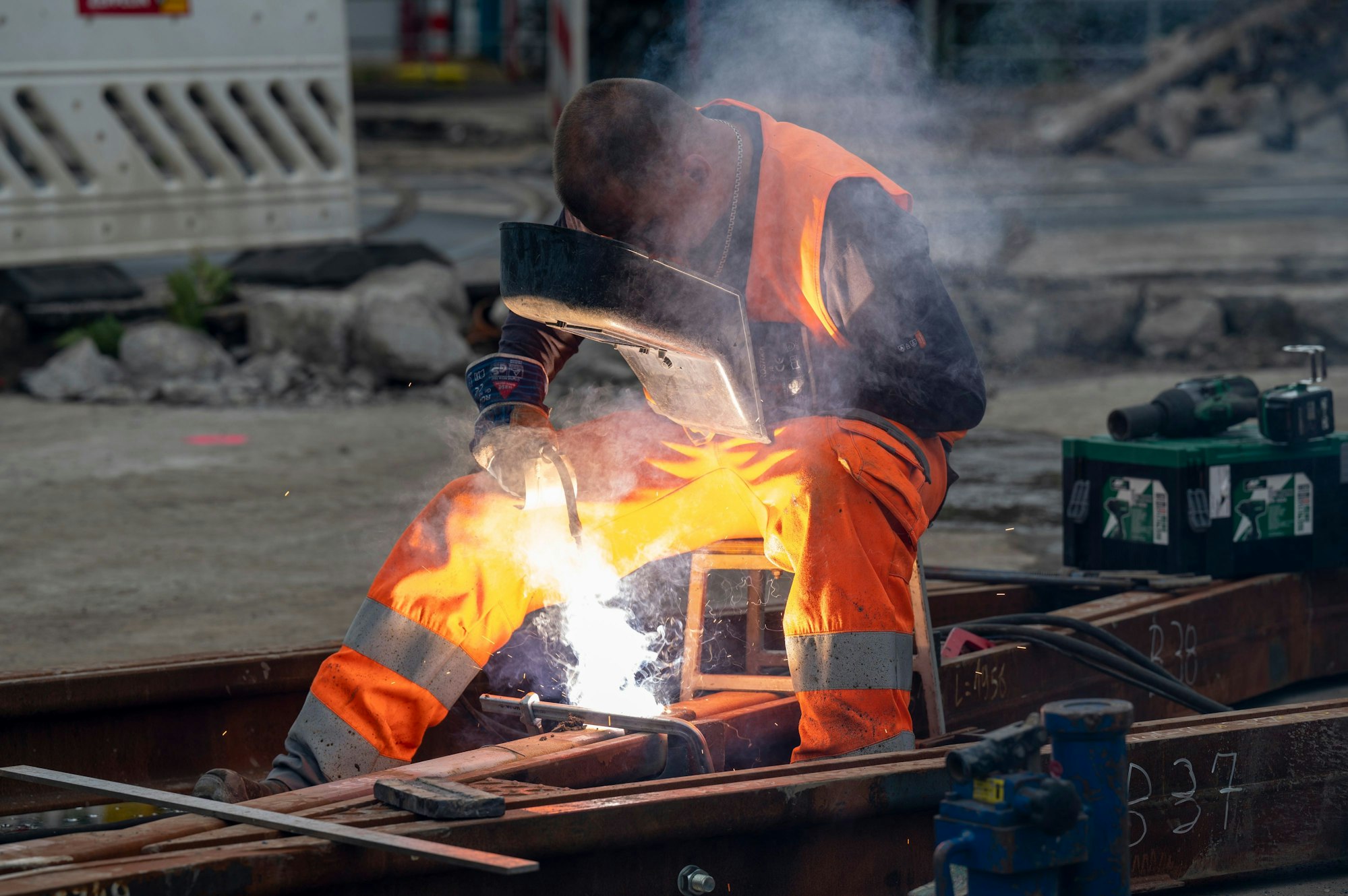 Ein Bauarbeiter schweißt zwei Gleise zusammen, helle Funken sprühen vom Gerät.