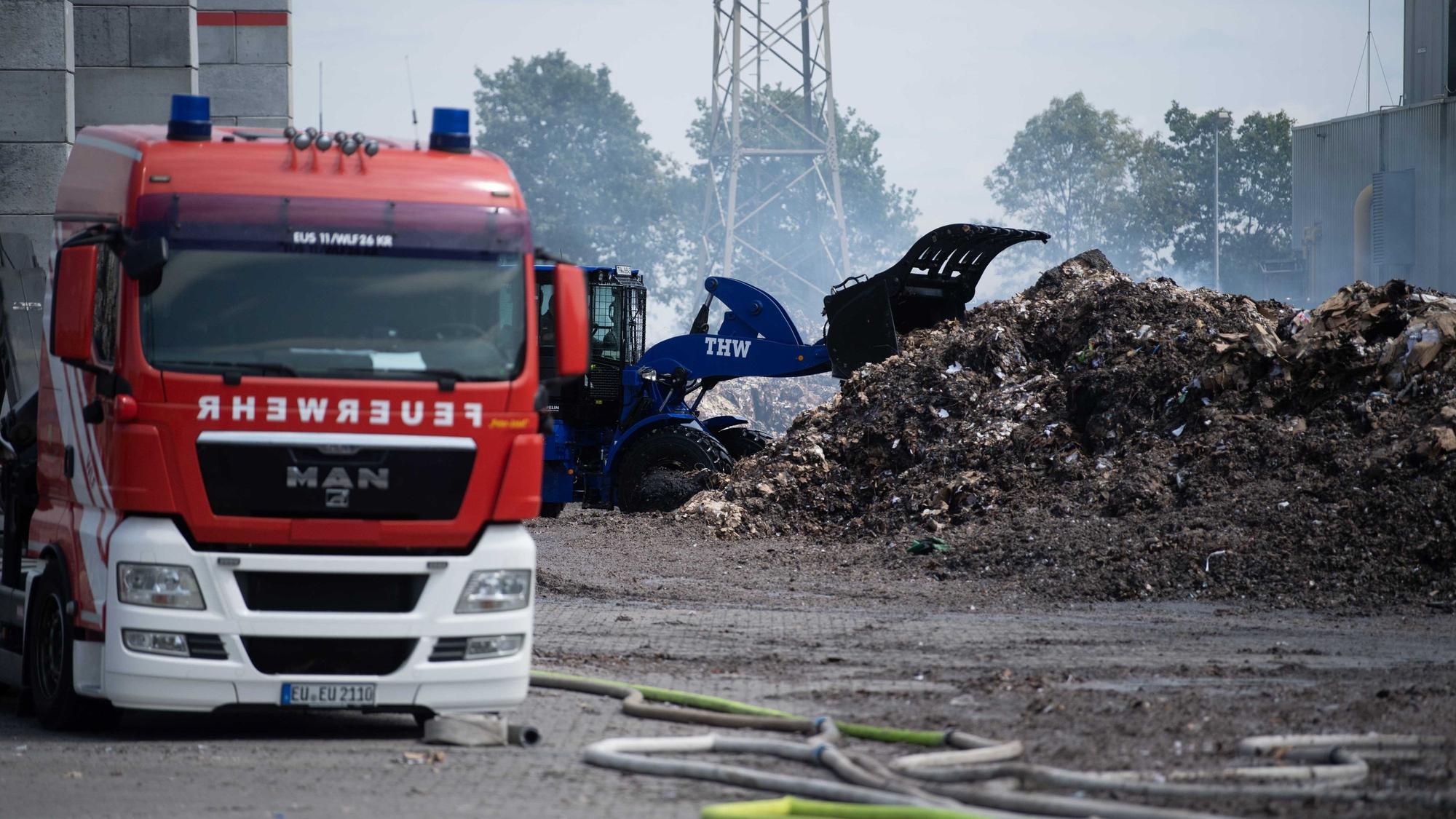 Ein Radler des THW zieht das abgelöschte Papier auseinander. Ein Feuerwehrfahrzeug ist im Vordergrund zu sehen.