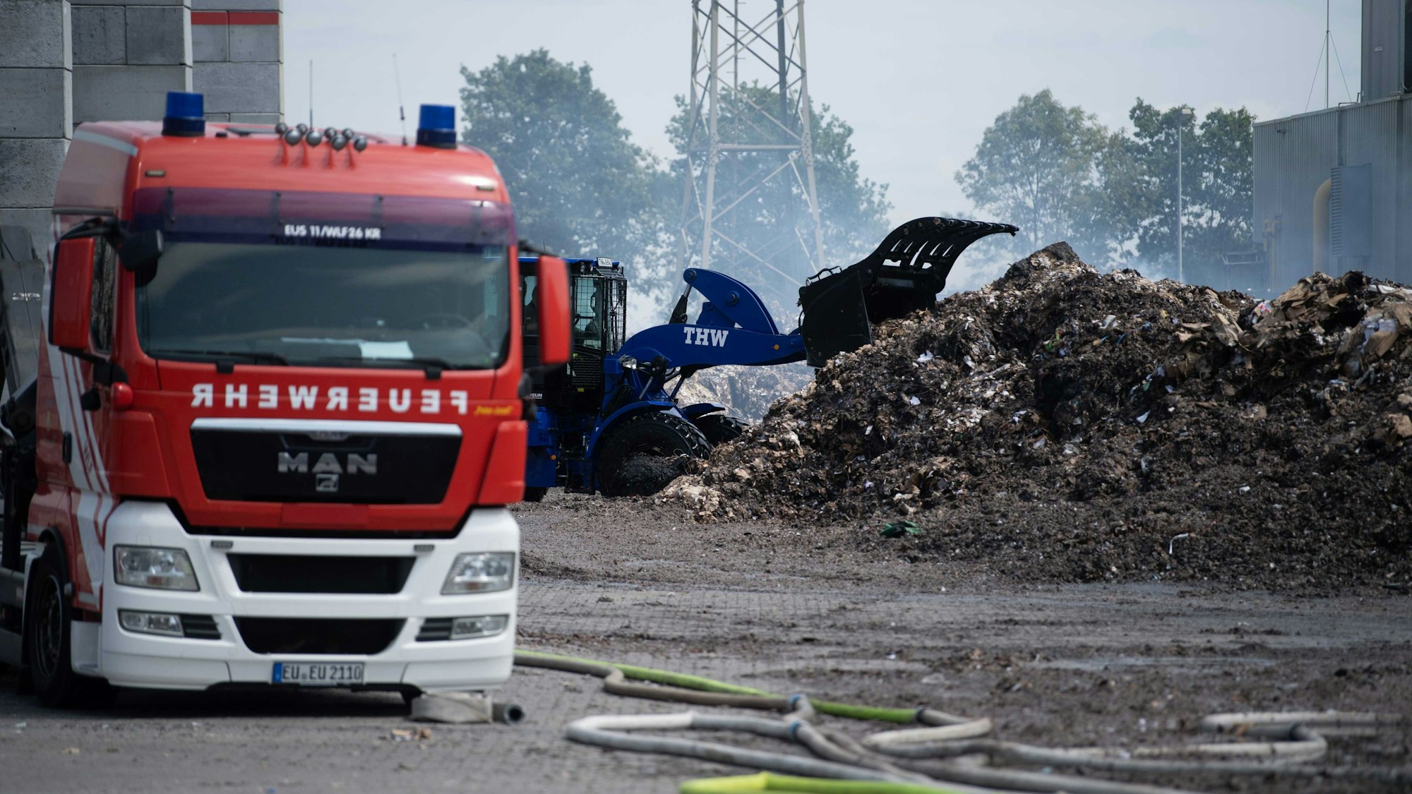 Ein Radler des THW zieht das abgelöschte Papier auseinander. Ein Feuerwehrfahrzeug ist im Vordergrund zu sehen.