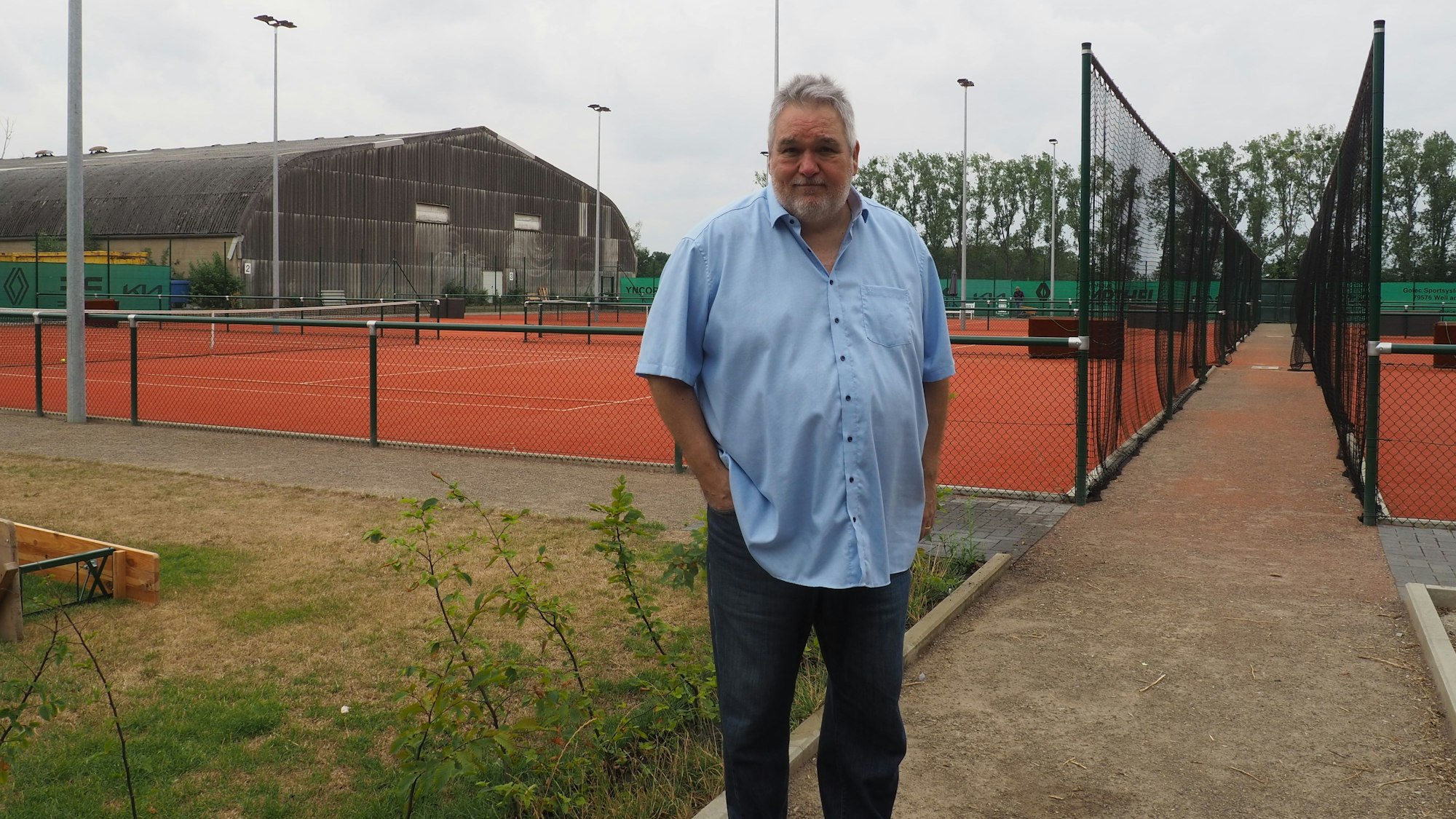 Ein Mann steht im Vordergrund, im Hintergrund sind Tennisplätze.
