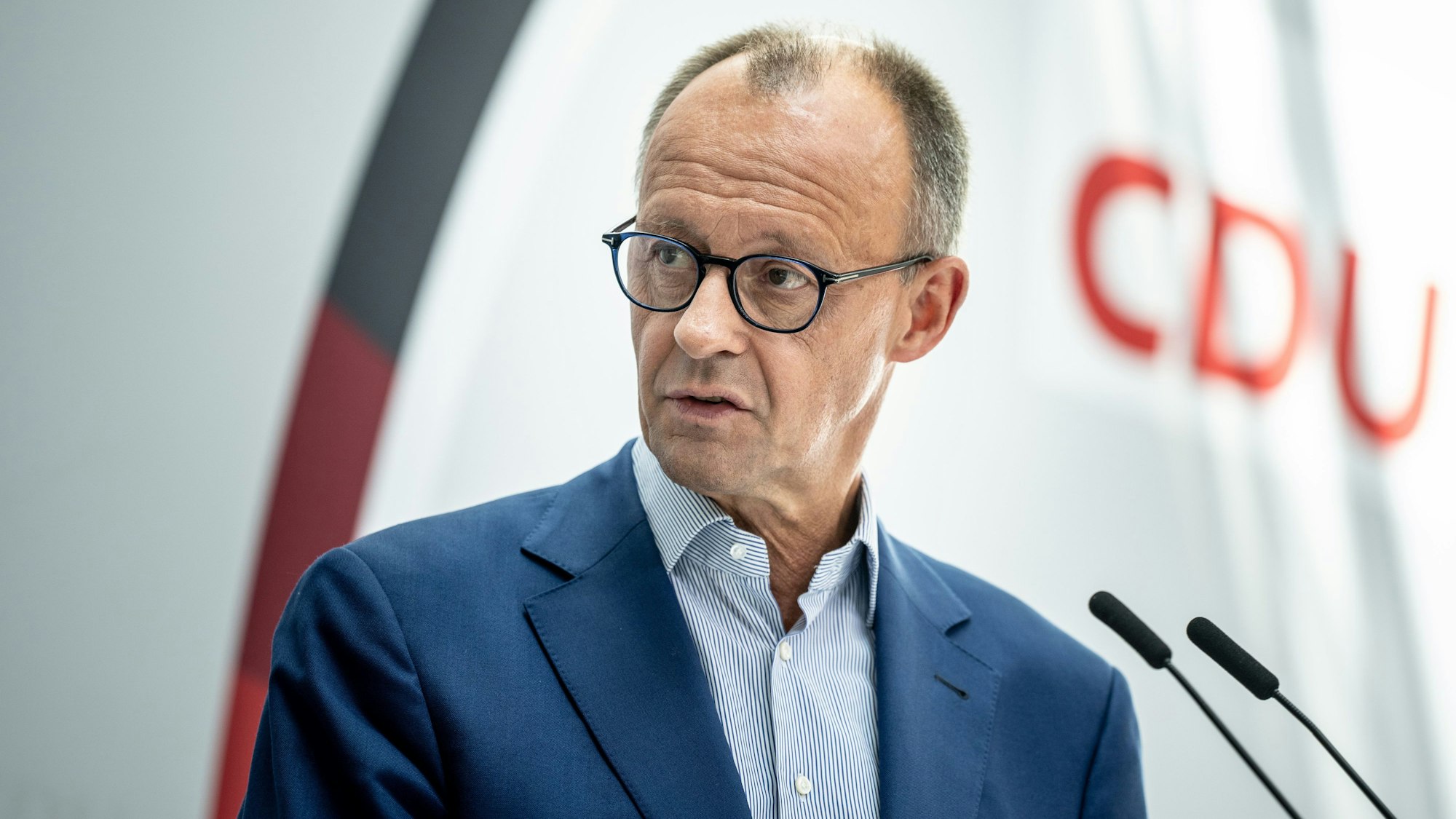 Friedrich Merz, CDU Bundesvorsitzender und Fraktionsvorsitzender der CDU/CSU Fraktion, steht auf einer Pressekonferenz an einem Rednerpult. Vor ihm befinden sich zwei Mikrofone. Hinter ihm hängt ein Plakat mit der Aufschrift „CDU“.