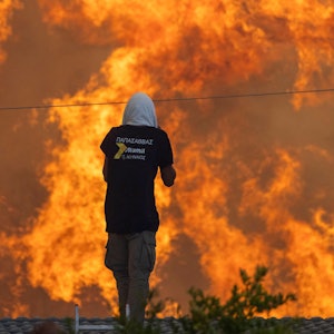 Zwei Männer stehen auf ihren Dächern vor riesigen Flammen und versuchen mit Wasserschläuchen ihre Häuser zu retten.