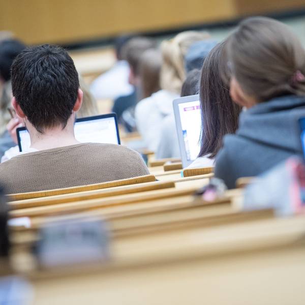 Studierende blicken in einem Hörsaal in ihre Laptops.