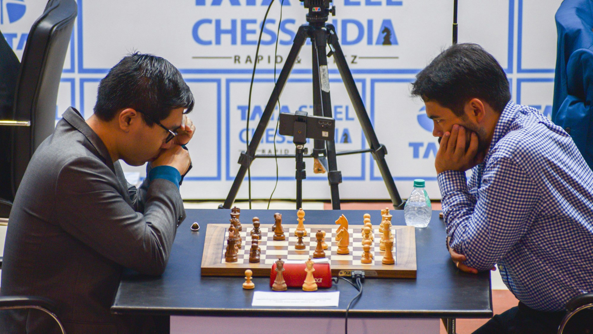 Die Kontrahenten sitzen sich in Denkposen gegenüber, wischen ihnen das Schachbrett. Ein Handy mit Stativ filmt das Brett.