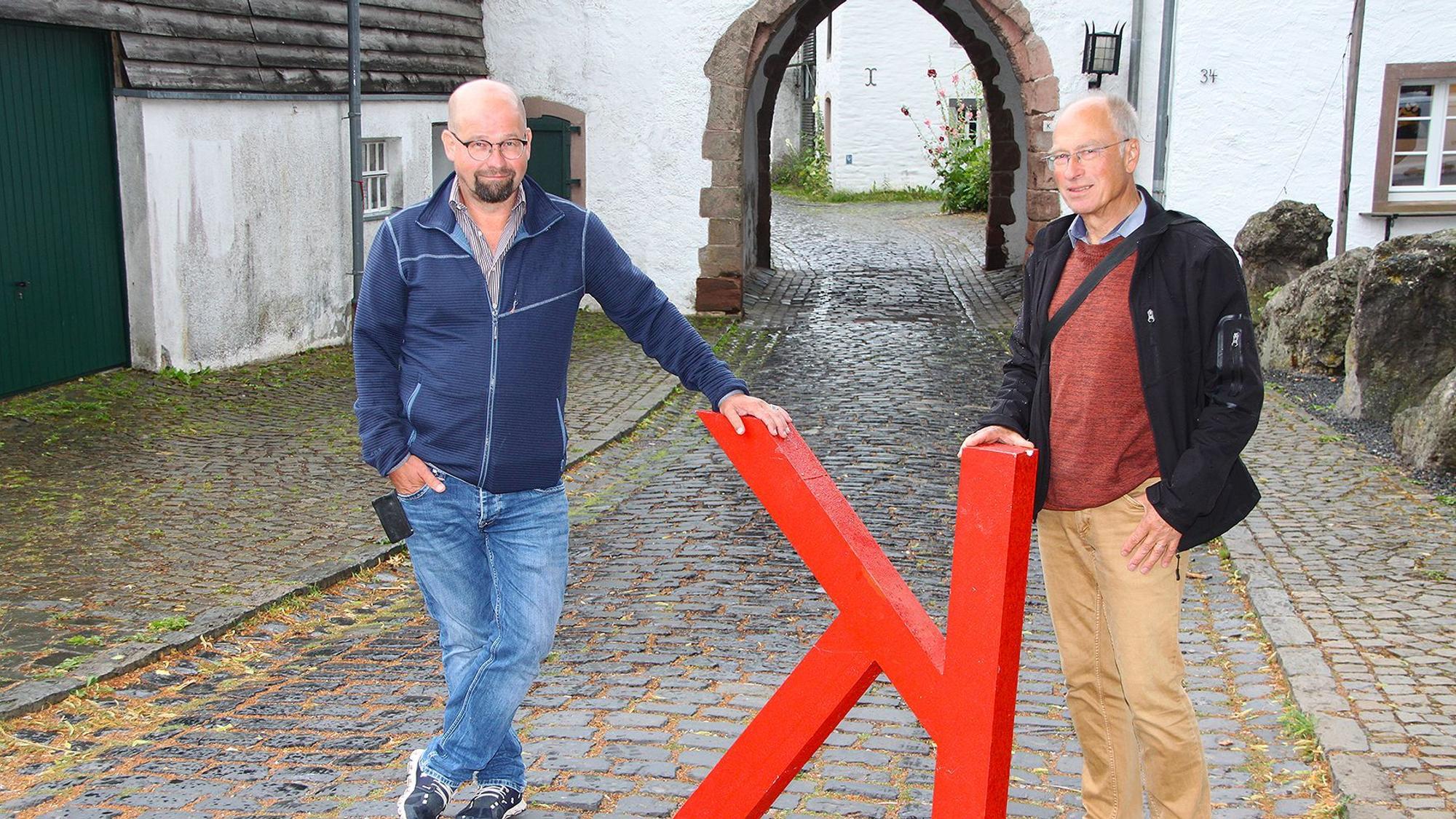 Die beiden Vertreter des Vereins Freies Forum Kronenburg mit einem auf dem Kopf stehenden K vor dem Nordtor des historischen Burgberings.