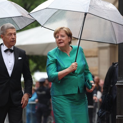 Bayern, Bayreuth: Ex-Bundeskanzlerin Angela Merkel (CDU) und Ehemann Joachim Sauer kommen mit Regenschirm zur Eröffnung der Richard-Wagner-Festspiele.