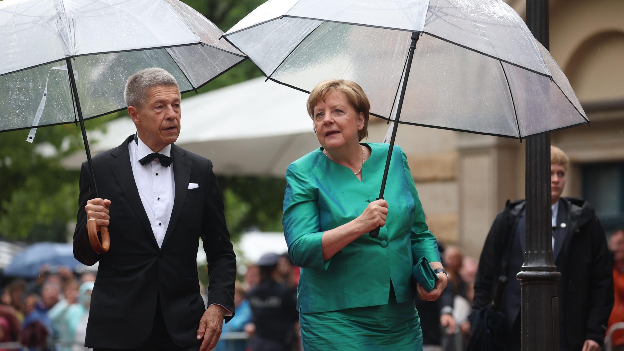 Bayern, Bayreuth: Ex-Bundeskanzlerin Angela Merkel (CDU) und Ehemann Joachim Sauer kommen mit Regenschirm zur Eröffnung der Richard-Wagner-Festspiele.