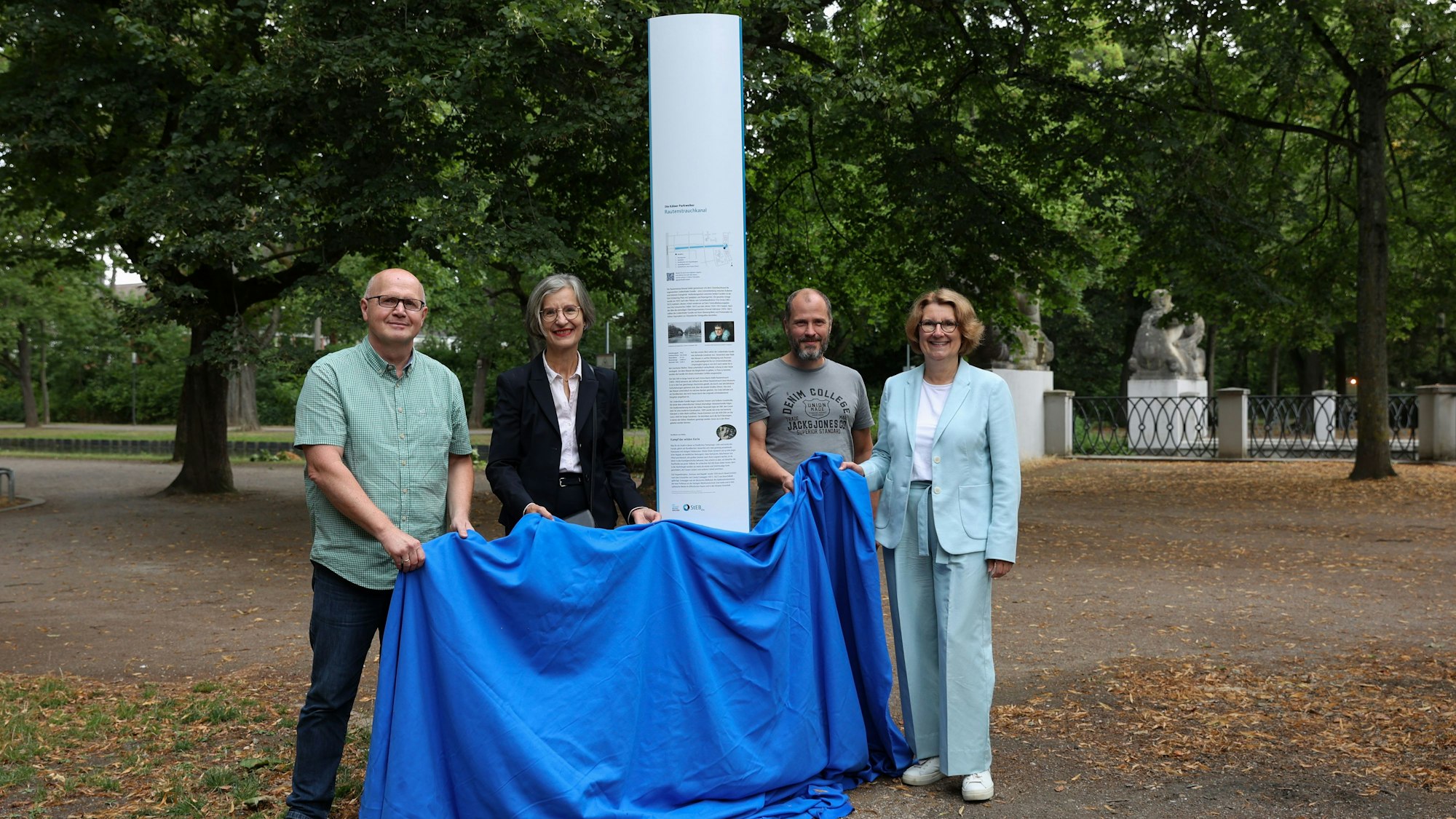 Stefan Schmitz (Projektleiter der StEB), Cornelia Weitekamp, Bezirksbürgermeisterin Köln-Lindenthal, Holger Weiffen (Projektleiter der StEB) und Ulrike Franzke, Vorständin der StEB Köln am Rautenstrauchkanal stehen vor der Infotafel.