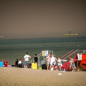 Touristen stehen an einem Strand, wohin sie wegen eines Waldbrandes auf der griechischen Insel Rhodos in Sicherheit gebracht worden sind. Die aktuelle Hitzewelle in Südeuropa lässt die Temperatur des Mittelmeers auf Höchstwerte steigen.