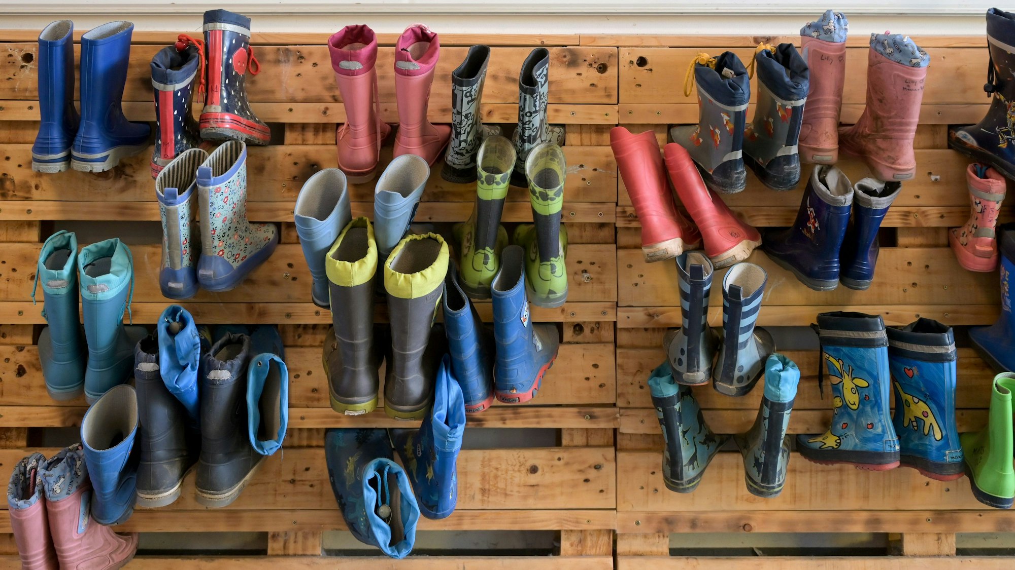 Gummistiefel hängen an einer Palettenwand in einer Kindertagesstätte.