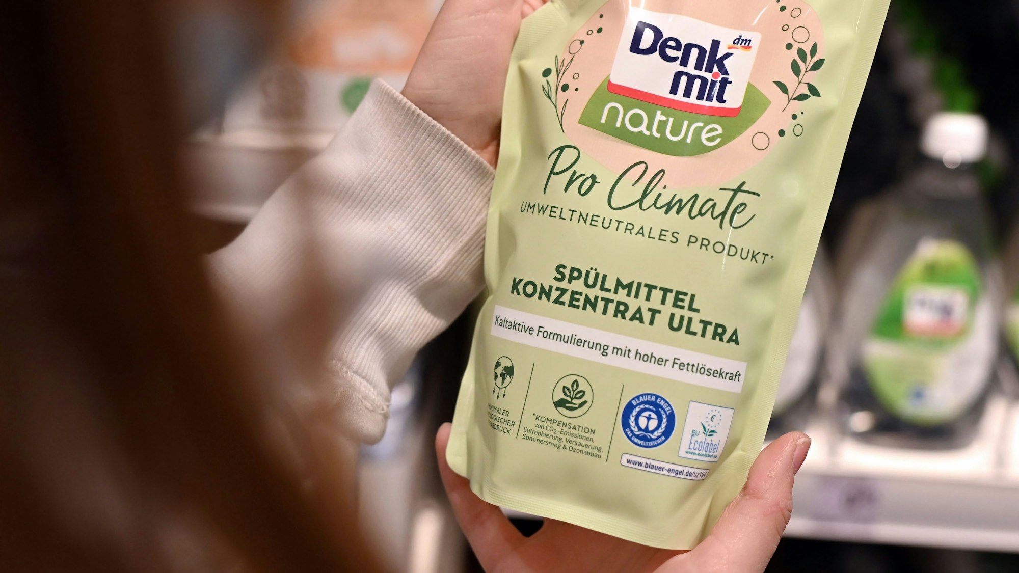 Eine Person betrachtet in einer Filiale der Drogeriemarktkette dm ein Produkt der dm Eigenmarke Denkmit, auf der «Pro Climate umweltneutrales Produkt» aufgedruckt ist.
