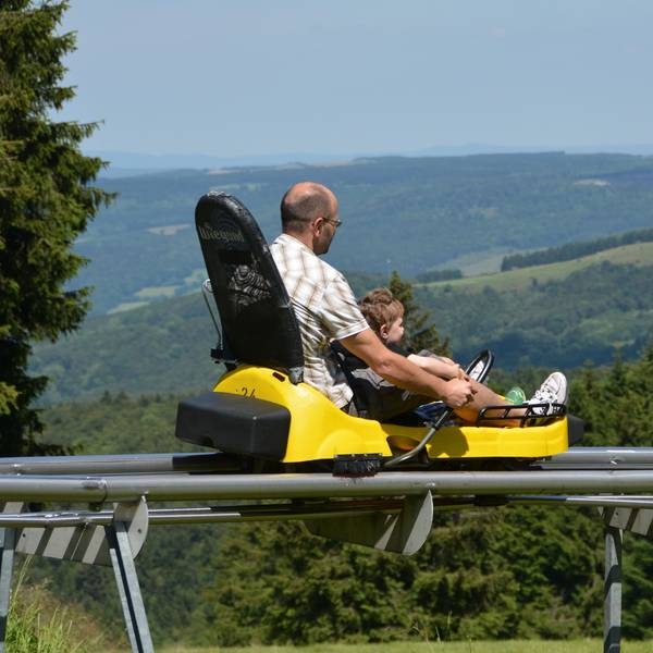 Ein Mann fährt mit einem Kind zusammen in einem Sommerrodelschlitten.
