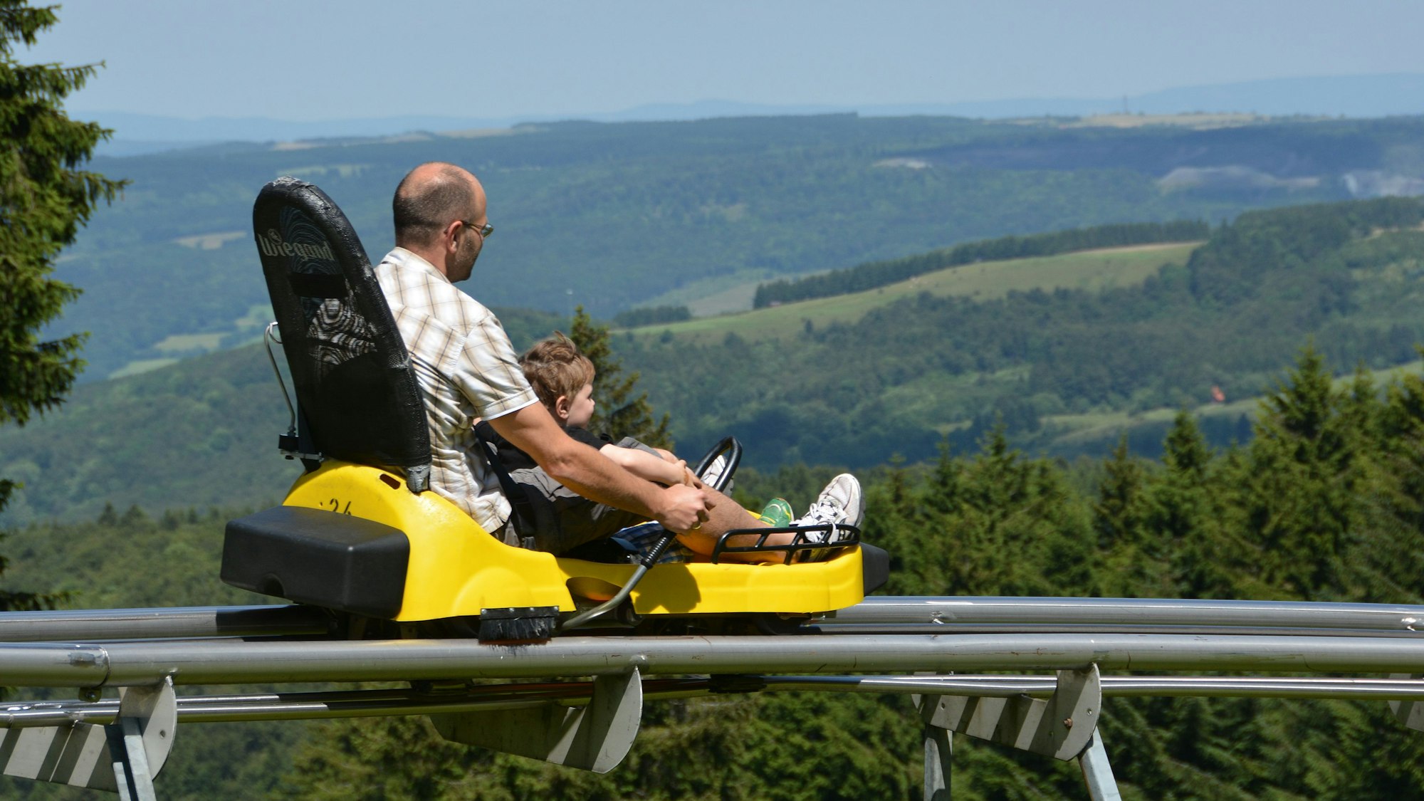 Ein Mann fährt mit einem Kind zusammen in einem Sommerrodelschlitten.