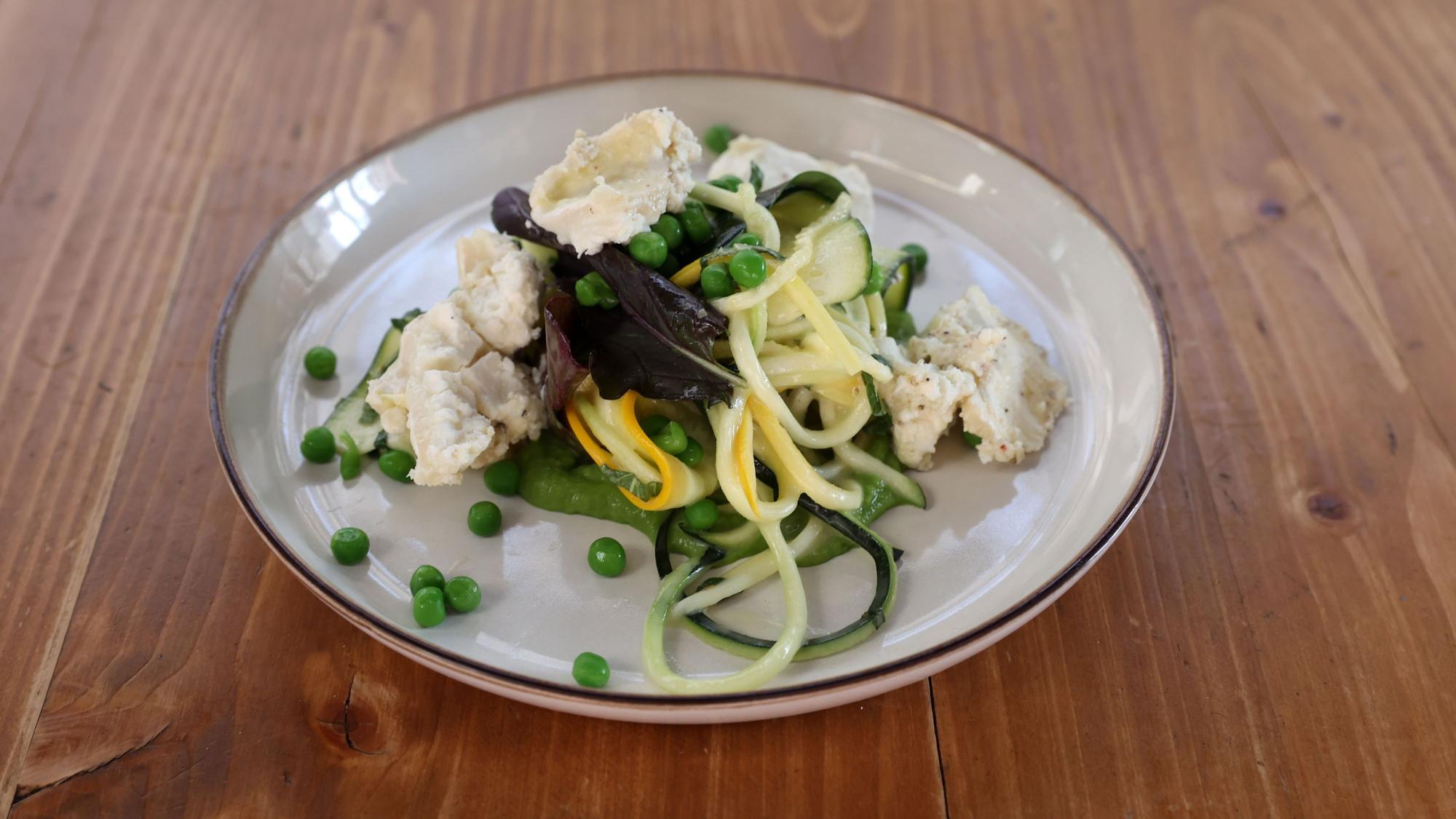 Zucchini-Nudeln, mit Erbsen und Ziegenkäse auf einem Teller angerichtet