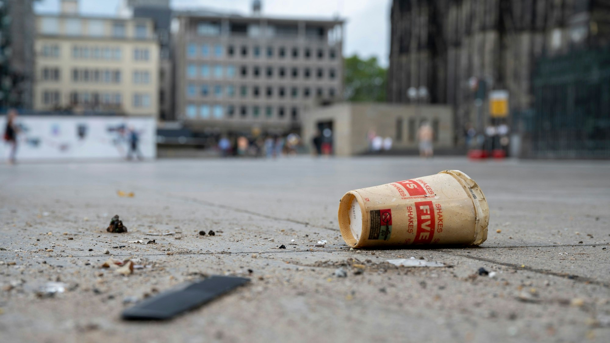 Eine Nahaufnahme des Bodens der Domplatte zeigt einen Wegwerfbecher und Schmutz.