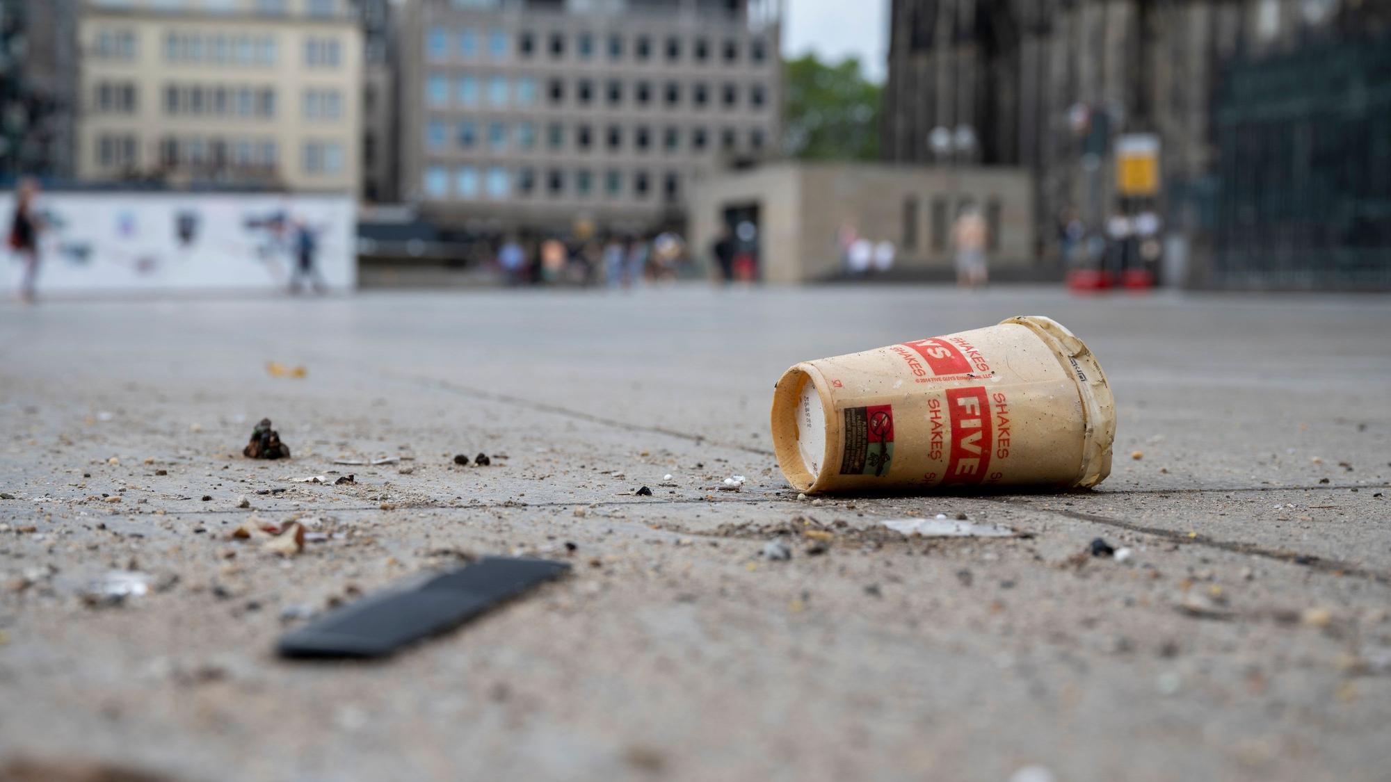 Ein Wegwerfbecher liegt am Kölner Dom am Boden.