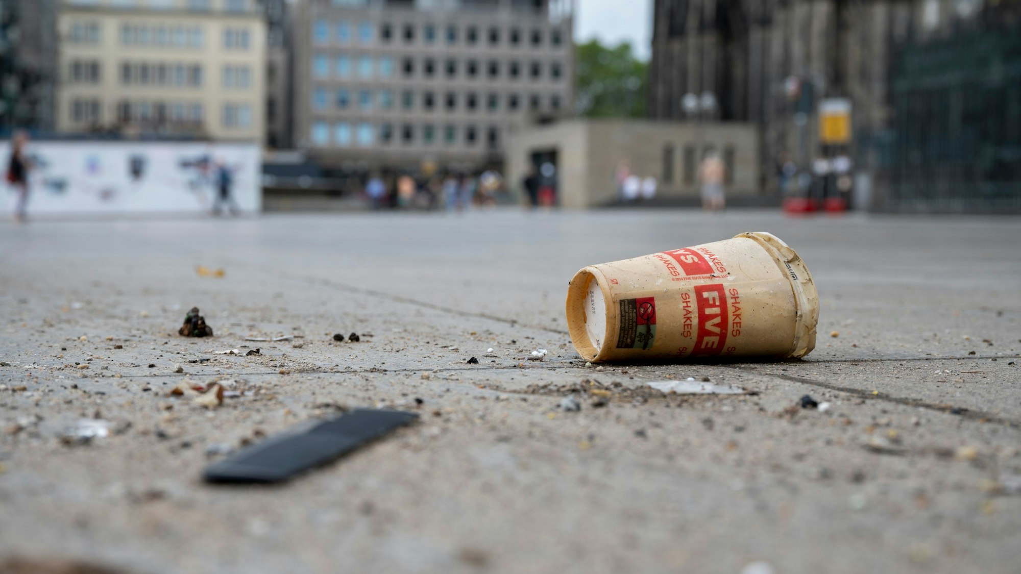 Ein Wegwerfbecher liegt am Kölner Dom am Boden.