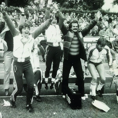 Spielerinnen und Trainer springen jubelnd am Spielfeldrand von einer Bank auf.