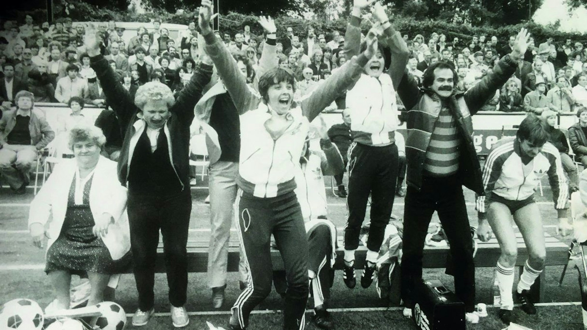 Spielerinnen und Trainer springen jubelnd am Spielfeldrand von einer Bank auf.