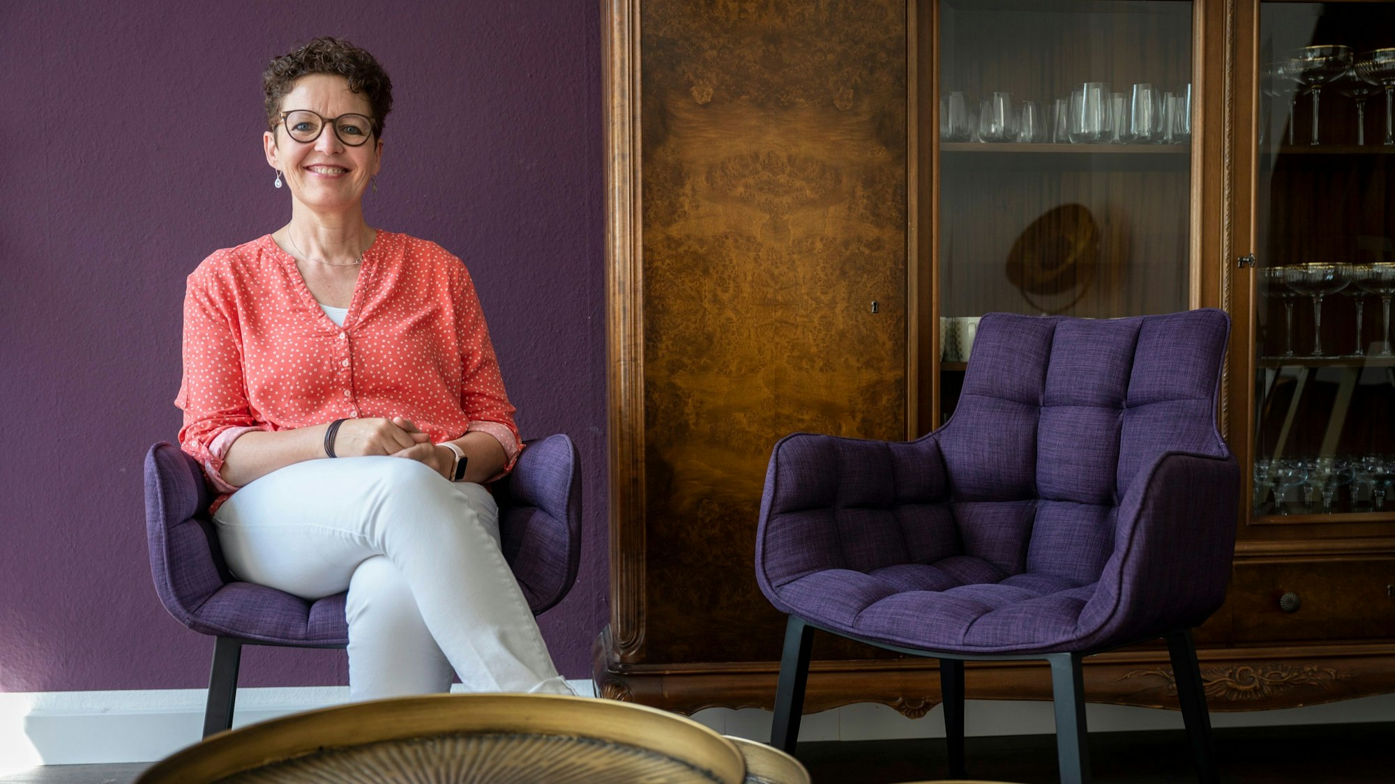 Silke Lemhöfer sitzt auf einem lilafarbenen Stuhl in ihrer Heilpraxis für Frauen