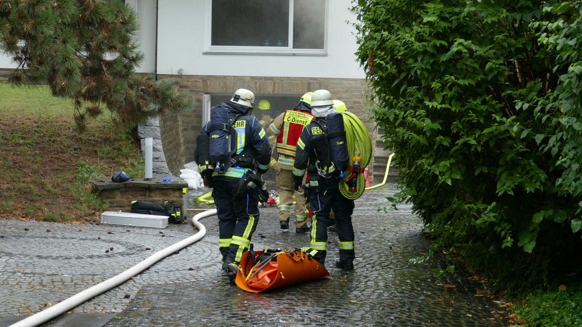Feuerwehrleute nähern sich einem verrauchten Haus.