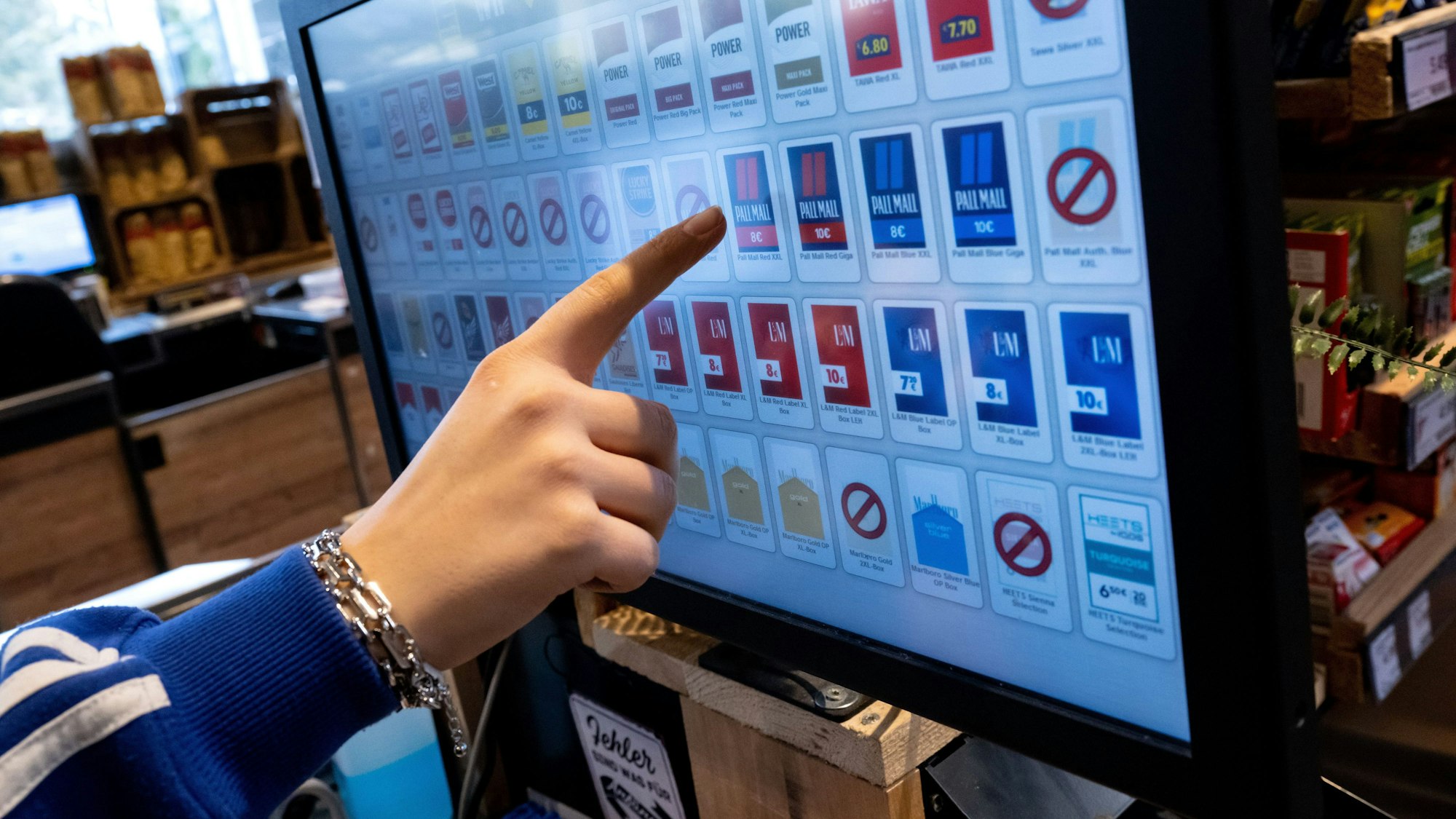 Eine Frau tippt an der Kasse eines Supermarktes mit dem Finger auf das Display von einem Zigarettenautomaten.