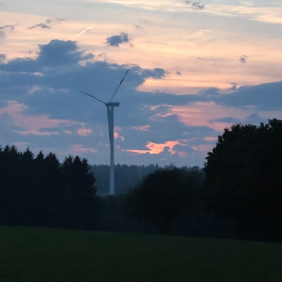 Ein Windrad dreht sich im Sonnenuntergang im Wald.