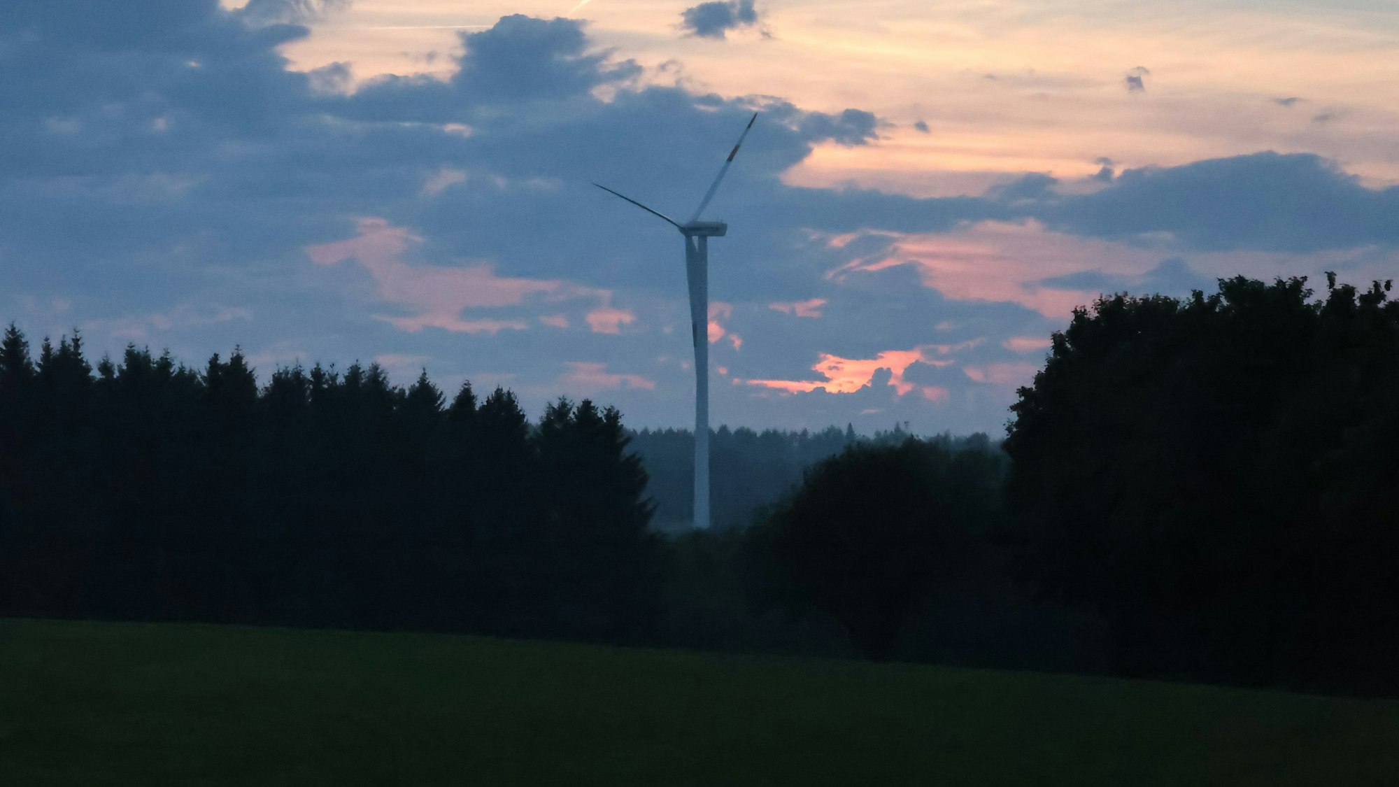 Ein Windrad dreht sich im Sonnenuntergang im Wald.